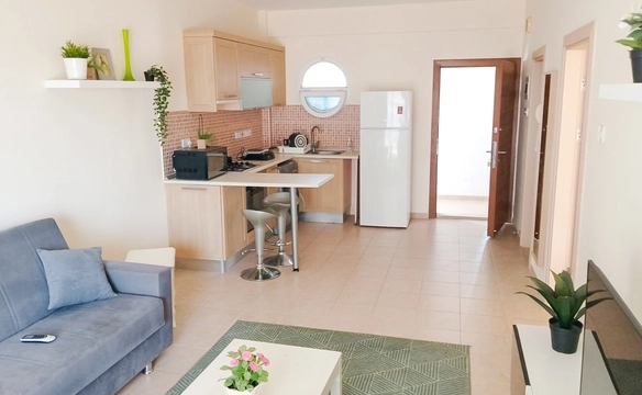 Fully equipped kitchen in a compact 1-bedroom apartment, featuring built-in wooden cabinets, washing machine, gas stove, fridge, and breakfast bar — located in Caesar Resort, North Cyprus.
